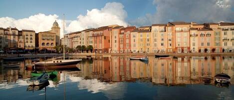 A waterfront with buildings reflecting in calm water, a dock with boats, and a clear sky.