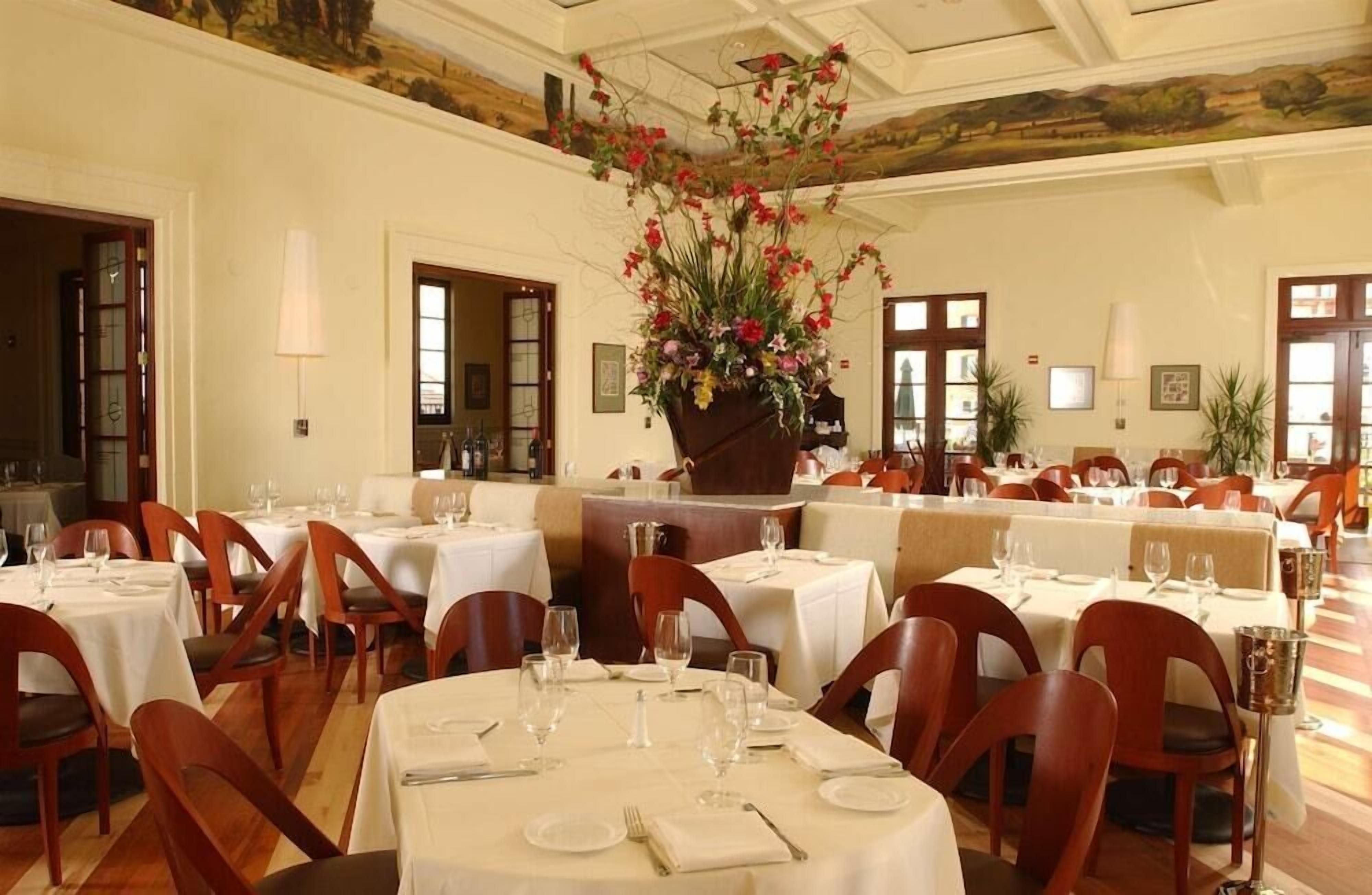 Un espace repas avec des tables rondes, des chaises et un grand arrangement floral en guise de décoration centrale.