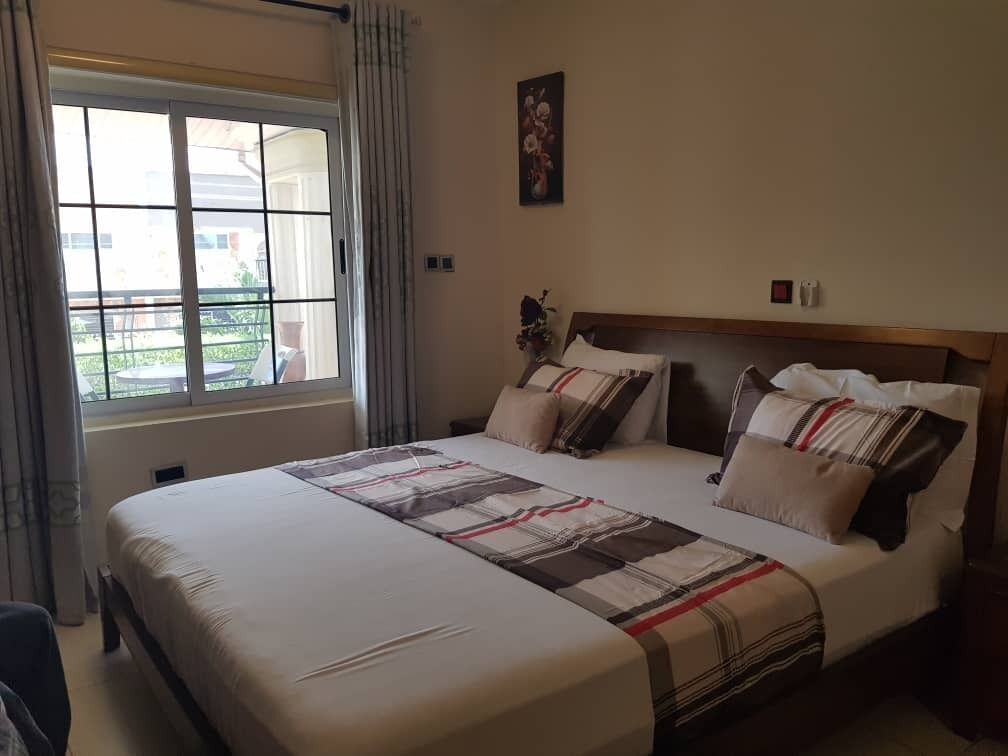 Habitación de hotel con una cama grande, una ventana con cortinas, una obra de arte en la pared y una mesita con un jarrón.