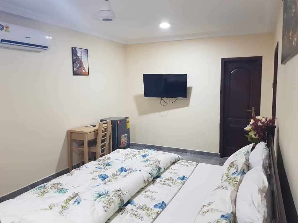 A hotel room with a bed, a desk, a chair, a TV mounted on the wall, and a door.