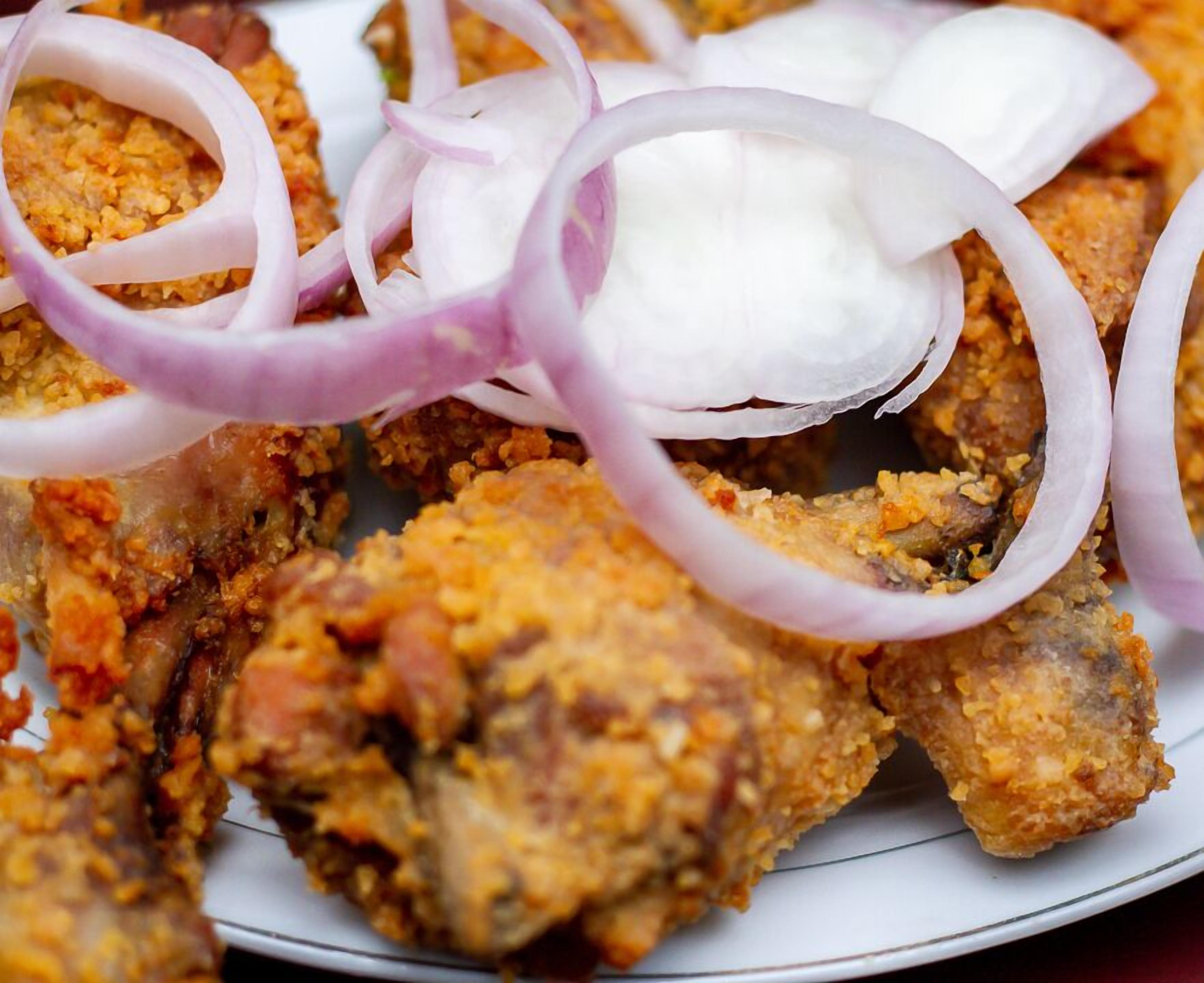 A plate of fried chicken with crispy batter, garnished with sliced red onions and a dollop of white sauce.