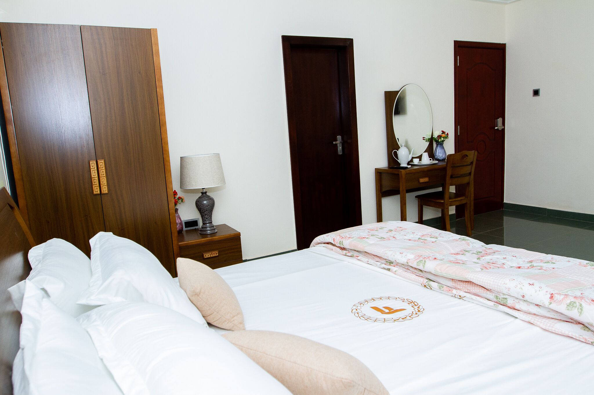 Een hotelkamer met een bed, een houten garderobe, een bureau met spiegel en een stoel.