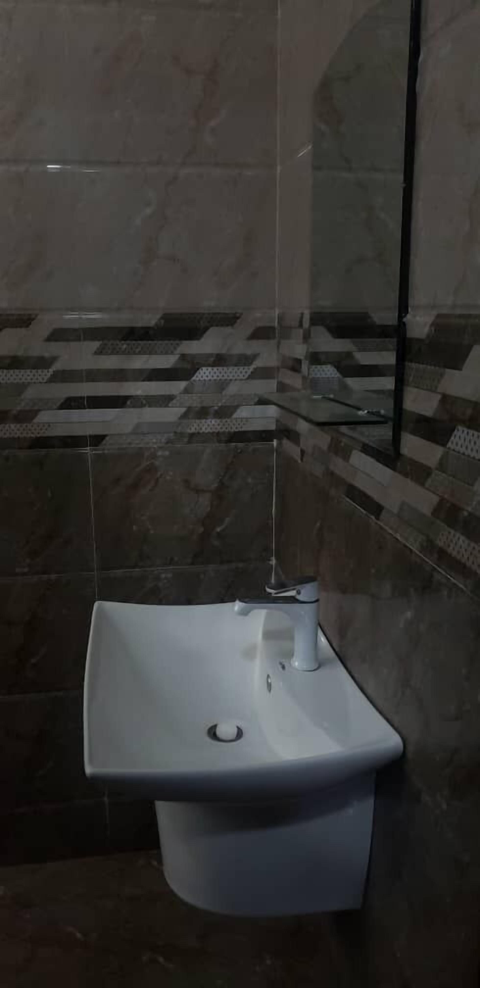 Une salle de bain avec un lavabo sur colonne blanc, un miroir et des murs carrelés.