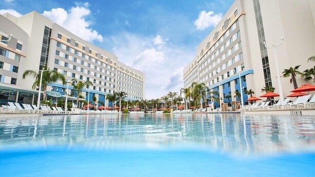 A hotel with a large pool, palm trees, and lounge chairs.