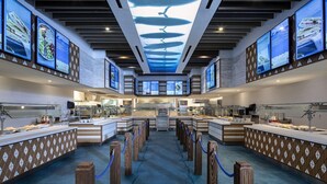A modern hotel lobby with a central reception desk, multiple screens displaying menus, and a unique ceiling design.
