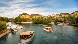 A river with boats and a hotel with multiple buildings and palm trees. - 2-Bedroom Suite at a 4⭐️ Hotel (Orlando)