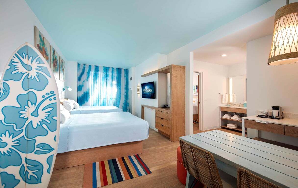A hotel room with a bed, a desk, a chair, a TV, and a bathroom visible through an open door.