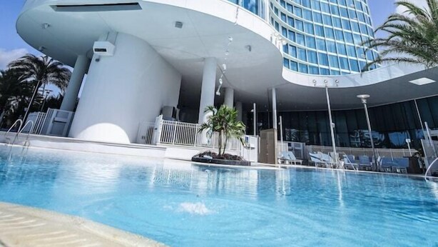 A modern hotel with a curved glass facade, a pool area, and palm trees. - 2-Bedroom Suite at a  Hotel (Orlando)