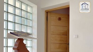 Eine Holztür mit Fußmatte, ein Fenster mit geometrischem Muster und ein Logo in der oberen rechten Ecke.