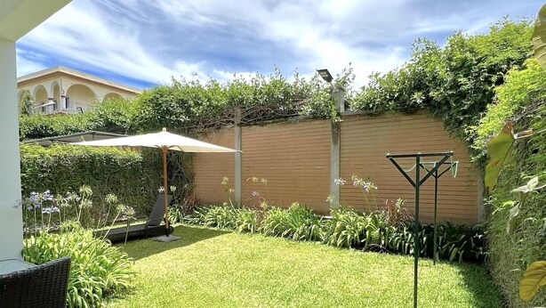 Ein gepflegter Innenhof mit Rasenfläche, Holzzaun und einer Pergola mit weißem Sonnenschirm.