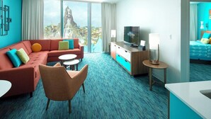 Une chambre d’hôtel moderne dotée d’une grande fenêtre offrant une vue sur une montagne et une cascade. On y trouve un canapé, un fauteuil, une petite table, un téléviseur et une table de chevet avec une lampe.