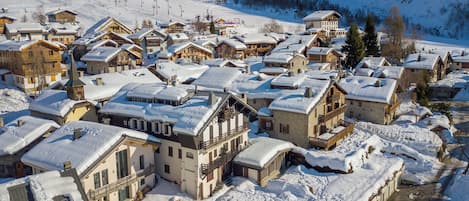 A snow-covered village with traditional wooden houses, a ski lift in the background, and a mountain in the distance.