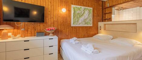 Une chambre d’hôtel avec un mur en bois, un téléviseur à écran plat, un lit avec du linge de maison blanc, une table de chevet avec une lampe et une carte encadrée accrochée au mur.
