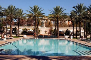 Ein Swimmingpool, umgeben von Palmen und Liegestühlen, mit einem Gebäude im Hintergrund.
