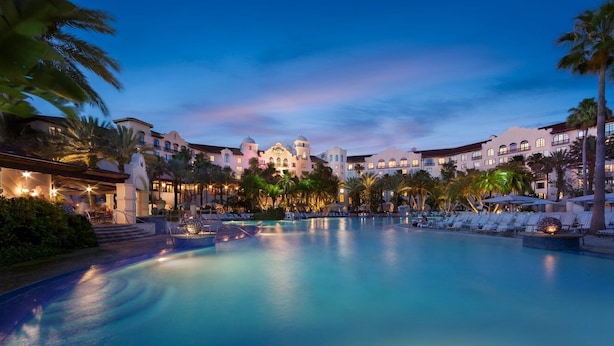 A resort with a large pool, palm trees, and a building with multiple balconies.