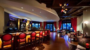 Un espace bar avec des chaises à revêtement rouge, un comptoir et un coin salon avec des chaises à motifs.