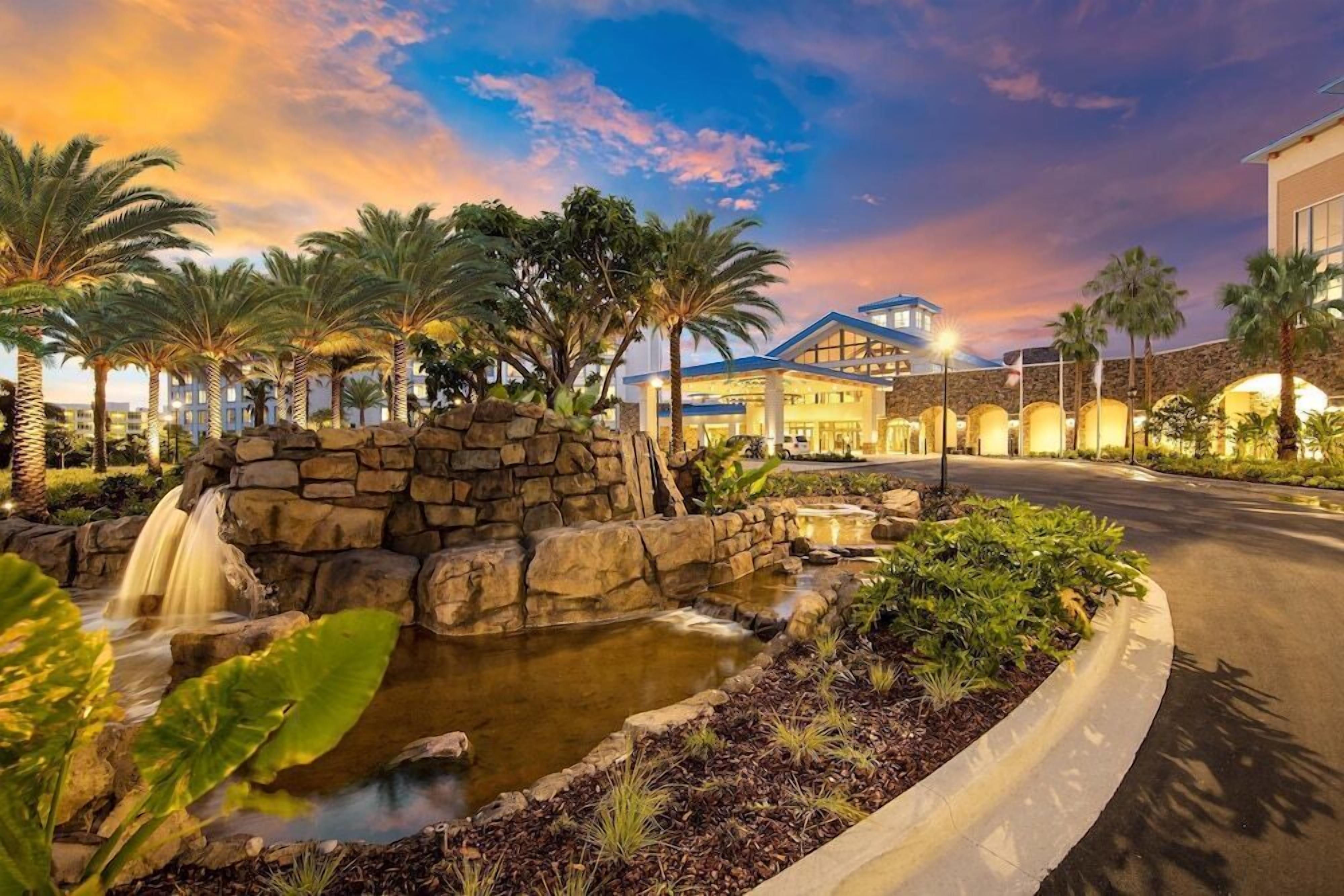 A hotel with a stone waterfall and palm trees, featuring a large building with a blue roof and a stone facade.