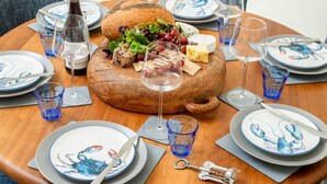 A round wooden table set for a meal with plates, cutlery, glasses, and a bottle of wine. - Lobster House by Interhome (Newquay)