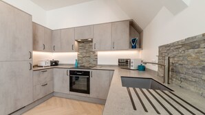 A modern kitchen with grey cabinets, a stone backsplash, and a built-in oven. - Lobster House by Interhome (Newquay)