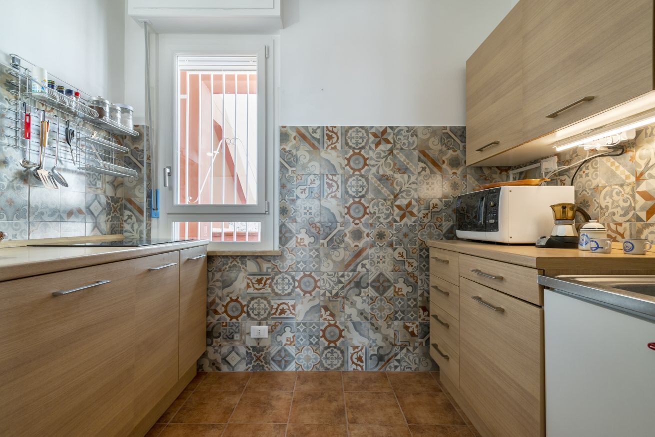 Cocina pequeña con ventana, baldosas estampadas y electrodomésticos básicos.
