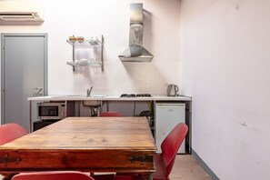 Una cocina compacta con una mesa de madera, sillas rojas, un microondas, lavavajillas y una campana extractora de acero inoxidable.