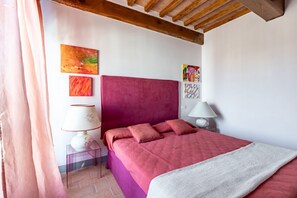 A bedroom with a red bed, two bedside lamps, and a wooden ceiling.
