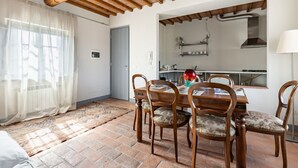 Ein Essbereich mit Holztisch und -stühlen, durch eine offene Tür ist eine Küche erkennbar, und ein Teppich mit Muster liegt auf dem Boden.