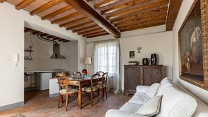 Ein Essbereich mit Holztisch und Stühlen, eine Küche im Hintergrund, ein weißes Sofa und ein Bild an der Wand.