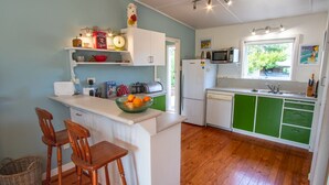 Cocina compacta con taburetes de madera, microondas, lavamanos y ventana con vistas a la vegetación.