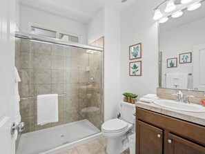 A modern bathroom with a glass-enclosed shower, a toilet, a sink with a mirror, and framed plant pictures on the wall.