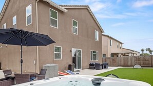Un jardin à l’arrière d’une maison, aménagé avec un jacuzzi, du mobilier d’extérieur et un parasol de patio.