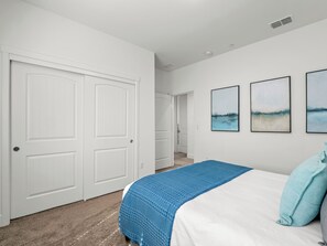 A bedroom with a bed, a blue blanket, and a light blue pillow. There are three framed pictures on the wall.