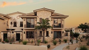 A multi-story residential building with balconies, a stone facade, and a landscaped garden. - Beautiful Golf or Family Luxury Villas Dunes 1913 (Palmilla)