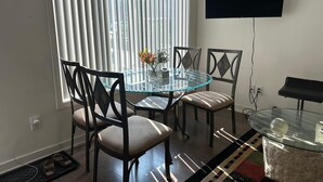 A modern dining area with a glass table and chairs, a flat-screen TV mounted on the wall, and a window with blinds. - Stylish 1BD Townhome. Dedicated Workspace, High-Speed Wi-Fi & Fast Transit (Toronto)