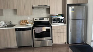A modern kitchen with stainless steel appliances, wooden cabinets, and a black countertop. - Stylish 1BD Townhome. Dedicated Workspace, High-Speed Wi-Fi & Fast Transit (Toronto)