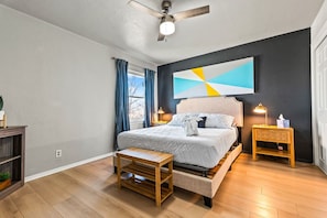 A modern bedroom with a bed, bedside tables, a bench, and a ceiling fan.
