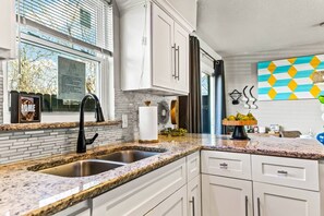 A kitchen with white cabinets, granite countertops, a stainless steel sink, a black faucet, and a window with blinds.