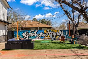 A backyard with a mural, outdoor seating, and a lawn. - Stylish & Comfy Downtown Gem ~ Workspace ~ Parking (Irving)