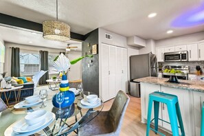A modern kitchen with stainless steel appliances, a dining area with a glass table, and a living room with a sofa and curtains.