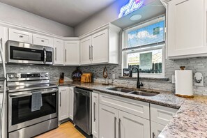 A modern kitchen with stainless steel appliances, white cabinetry, a granite countertop, and a window with blinds.