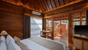 A wooden room with a bed, a TV, and a dining area with a table and chairs. - Unagi Wooden Villa by Emana (Ubud)