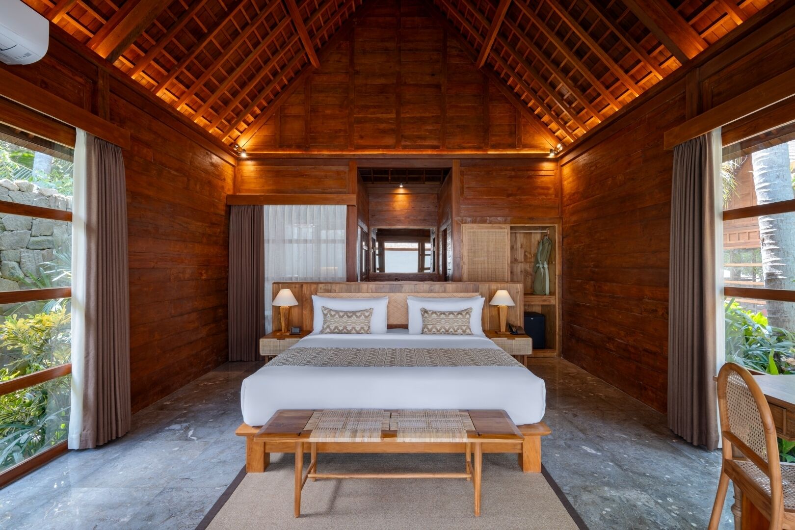 Ein Zimmer aus Holz mit einem großen Bett, Nachttischlampen und Blick auf Grün.