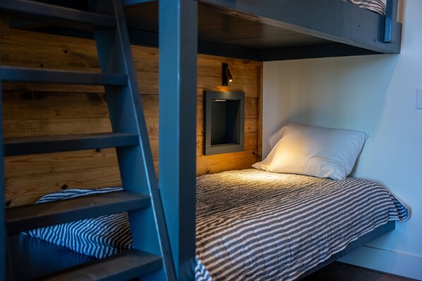 A bunk bed with a ladder, a bedside table, and a wall-mounted light fixture.