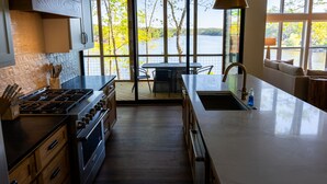 Uma cozinha moderna com uma ilha grande, uma sala de jantar com vista para um lago e um espaço de estar aconchegante com um sofá.