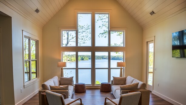 Ampla sala de estar com uma grande janela com vista para um lago, piso de madeira e um conjunto de sofás moderno.