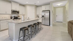 A modern kitchen with white cabinets, stainless steel appliances, a granite countertop, and bar stools. - Gated Community - Close to Beaches, Parks, Dining & Shops! Easy Walk to Community Pool! (Fort Myers)