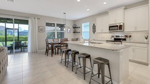 A modern kitchen with white cabinets, a large island with bar stools, and a view of the outdoors. - Gated Community - Close to Beaches, Parks, Dining & Shops! Easy Walk to Community Pool! (Fort Myers)
