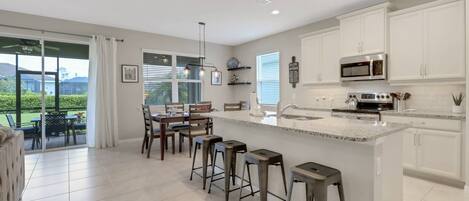 A modern kitchen with white cabinets, a large island with bar stools, and a view of the outdoors.