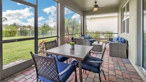 A covered patio with a table and chairs, large windows, and a ceiling fan. - Gated Community - Close to Beaches, Parks, Dining & Shops! Easy Walk to Community Pool! (Fort Myers)