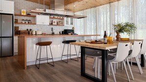 Une cuisine moderne avec des meubles blancs, un plan de travail en bois et un coin repas comprenant une table et des chaises.
